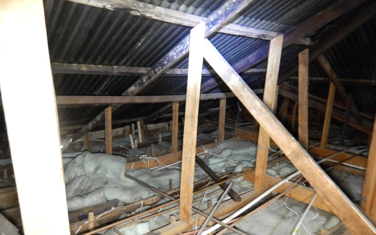 Timber roof structure seen from inside the roof space, beneath the original corrugated sheeting.
