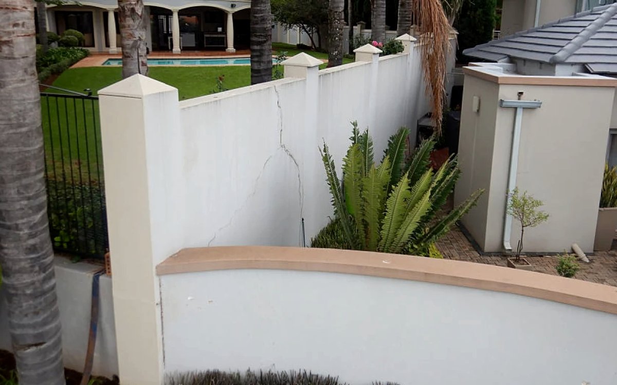 Cracking running from the coping down through a rendered masonry infill panel between the boundary wall's columns.